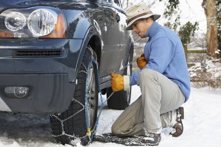 Man Putting Snow Chains Onto Tyre Of Carの写真素材