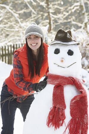 Young Woman Building Snowman In Gardenの写真素材