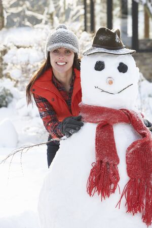 Young Woman Building Snowman In Gardenの写真素材