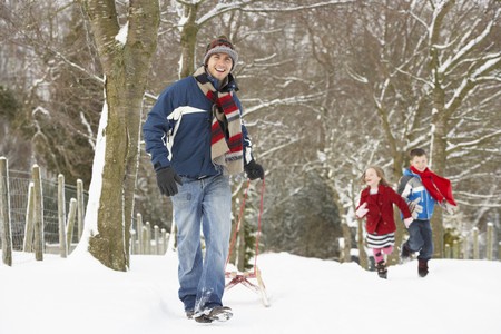 Father Pulling Children On Sledge Through Winter Landscapeの写真素材