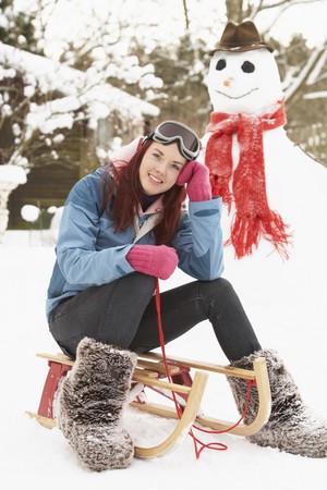 Teenage Girl With Sledge Next To Snowmanの写真素材