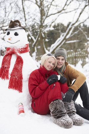 Teenage Couple In Winter Landscape Next To Snowman With Flask And Hot Drinkの写真素材