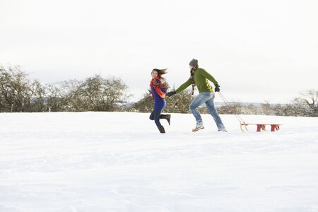 Teenage Couple Pulling Sledge Across Snowy Fieldの写真素材