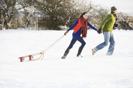 Teenage Couple Pulling Sledge Across Snowy Fieldの写真素材