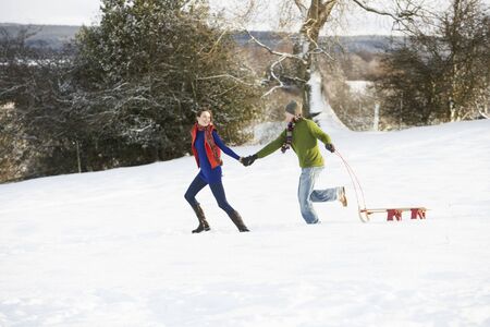 Teenage Couple Pulling Sledge Across Snowy Fieldの写真素材