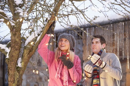 Two Teenage Girls Hanging Fairy Lights In Tree With Icicles In Foregroundの写真素材