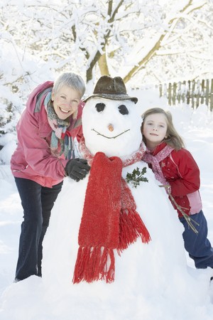 Young Girl With Grandmother Building Snowman In Gardenの写真素材