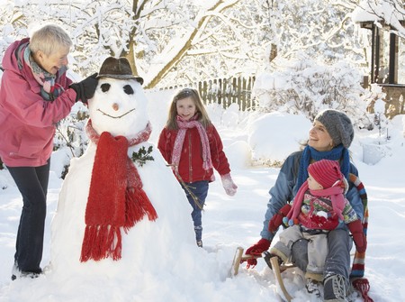 Young Girl With Grandmother And Mother Building Snowman In Gardenの写真素材
