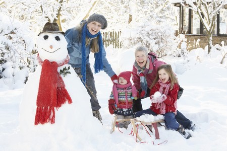 Young Girl With Grandmother And Mother Building Snowman In Gardenの写真素材