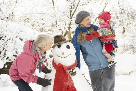 Young Girl With Grandmother And Mother Building Snowman In Gardenの写真素材