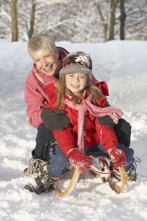 Young Girl With Grandmother Riding On Sledge In Snowy Landscapeの写真素材