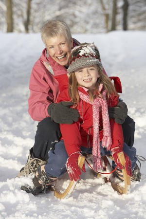 Young Girl With Grandmother Riding On Sledge In Snowy Landscapeの写真素材