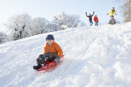 Young Boy Sledging Down Hill With Family Watchingの写真素材