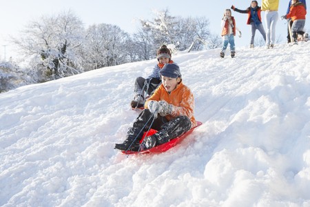 Young Boy Sledging Down Hill With Family Watchingの写真素材