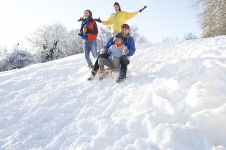 Family Having Fun Sledging Down Snowy Hillの写真素材