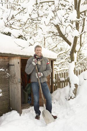 Middle Aged Man Clearing Snow From Path To Wooden Storeの写真素材