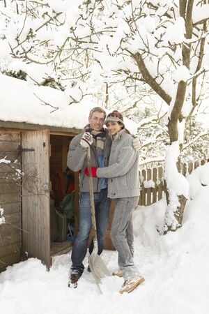 Young Couple Clearing Snow From Path To Wooden Storeの写真素材