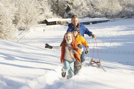 Father And Children Pulling Sledge Up Snowy Hillの写真素材