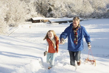 Father And Daughter Pulling Sledge Up Snowy Hillの写真素材