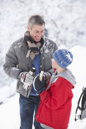 Father And Son Stopping For Hot Drink And Snack On Walk Through Snowy Landscapeの写真素材