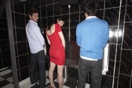 Woman and two men standing at mens urinalの写真素材