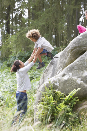 Father Helping Children To Jump Off Rocksの写真素材