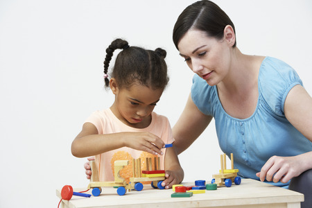 Teacher And Pre-School Pupil Playing With Wooden Houseの写真素材
