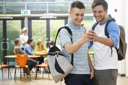Two Male Students In Classroom Reading Message On Phoneの写真素材