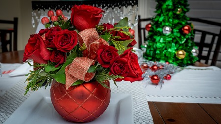 Christmas Rose Floral Arrangement on dining table with Christmas Tree ornament in backgroundの写真素材