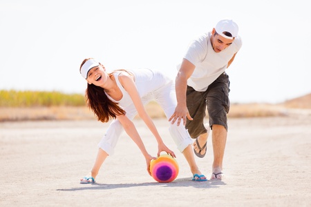 Happy young couple playing with colorful ball outdoors; white sky background and copy space.の写真素材