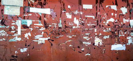 An iron bulletin board with torn paper ads at a bus stop.