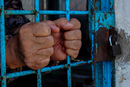 Man in prison hands of behind hold Steel cage jail bars. offender criminal locked in jail. The grate is locked from the outside.の写真素材
