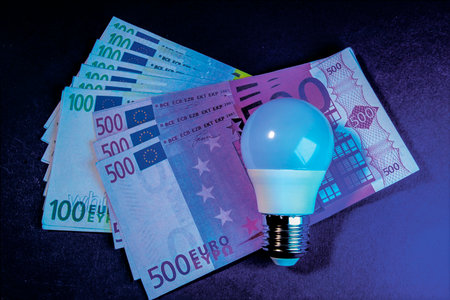 A light bulb on the surface of the euro currency. A symbol of the high cost of electricity in Europe.の写真素材