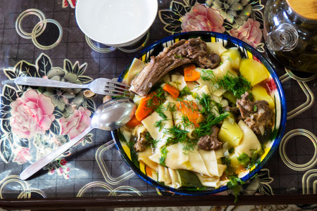 Traditional Central Asian dish âBeshbarmakâ with lamb, handmade noodles, potatoes, and carrots, garnished with fresh dill on a colorful plate.の写真素材