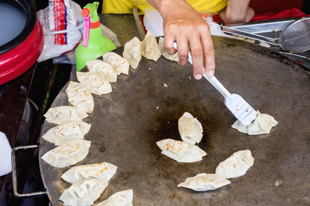 Fried Chinese dumplings on the big pan in Street food shop with maker's handの写真素材
