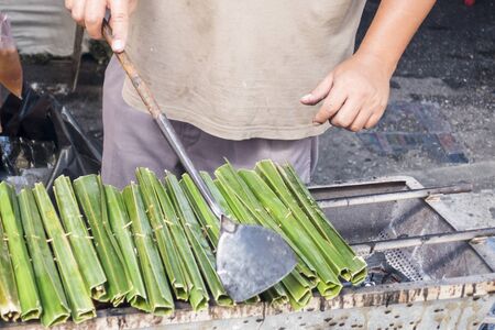 Man making thai dessert called "Kanom Jak" ,Thai sweetmeat made of flour, coconut and sugar in green leaf in street food shopの写真素材