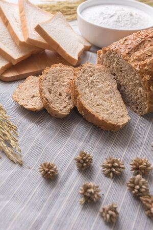 Freshly baked traditional wheat bread and wheat and  oat on white pattern linen tablecloth, soft focusの写真素材