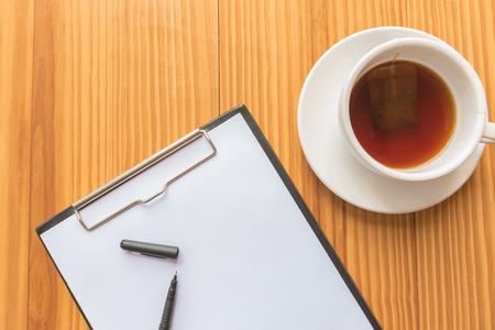 A cup of tea or coffee and a pen and notebook on wooden desks in officeの写真素材