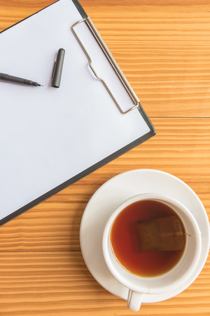 A cup of tea or coffee and a pen and notebook on wooden desks in officeの写真素材