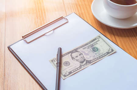 a pen and dollar bank placed on paper note and tea or coffee cup on the side on the wooden table background.の写真素材
