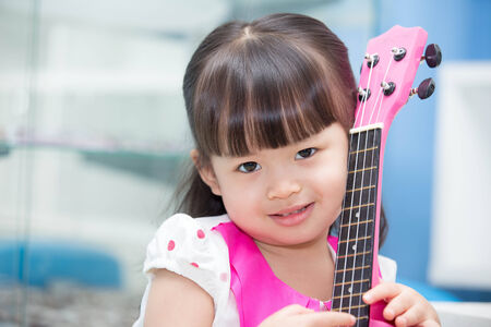 Asian girl sitting happily hugging pink ukuleleの写真素材