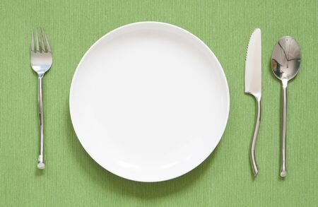 dinner place setting a white plate with silver fork and spoon greenの写真素材