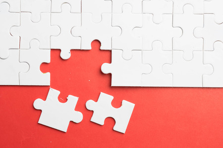 Put the last piece of jigsaw puzzle to complete the mission on red backgroundの写真素材