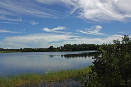 Blue Sky painted with white swirls over lakeの写真素材
