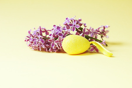 Minimalist Easter background with a bunch of lilac and painted eggs on a yellow background.の写真素材