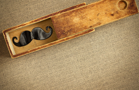 Fake mustache in an old wooden box on the tweed fabric. Retro styling. Focus is on the box.の写真素材