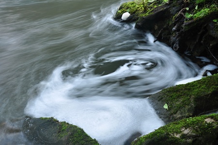 Blurred flowing river with a stone bank with rootsの写真素材