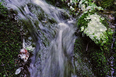 Small waterfall at spring creek with ice and green mossの写真素材