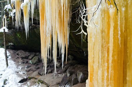 Frozen waterfalls on the rock, orange colored and snowの写真素材