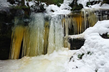 Frozen waterfalls on the rock, orange colored and snowの写真素材